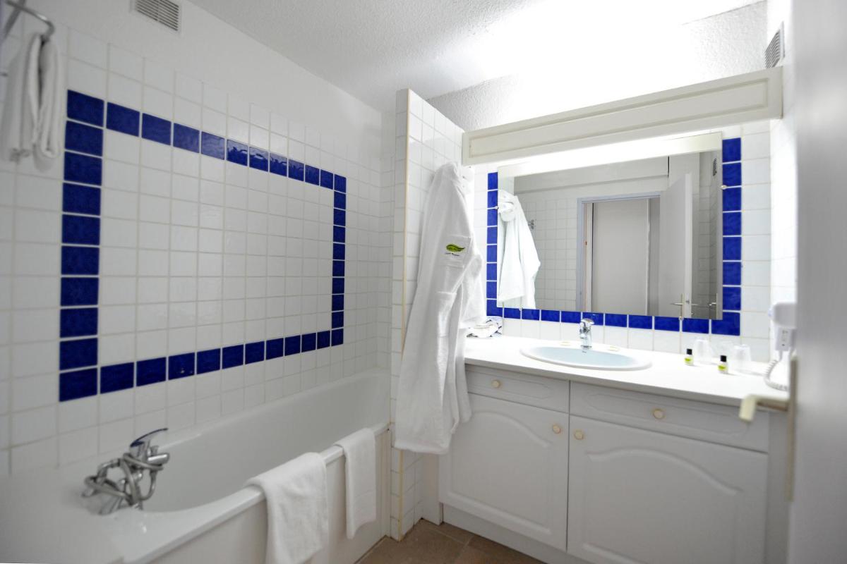 La salle de bains est pourvue de carrelage bleu et blanc, d'une baignoire et d'un lavabo. dans l'établissement Thalacap Camargue, à Saintes-Maries-de-la-Mer