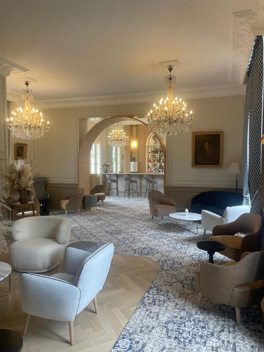 un grand salon avec des chaises, des tables et des lustres dans l'établissement Grand Hôtel "Château de Sully" - Piscine & Spa -Teritoria, à Sully