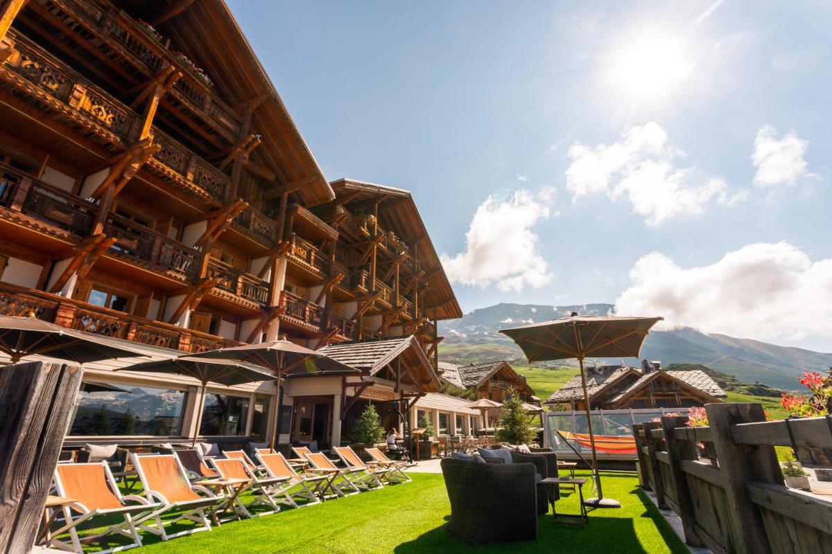 un complexe avec des chaises et des parasols sur la pelouse dans l'établissement Hôtel Au Chamois d'Or by Les Etincelles, à L'Alpe-d'Huez