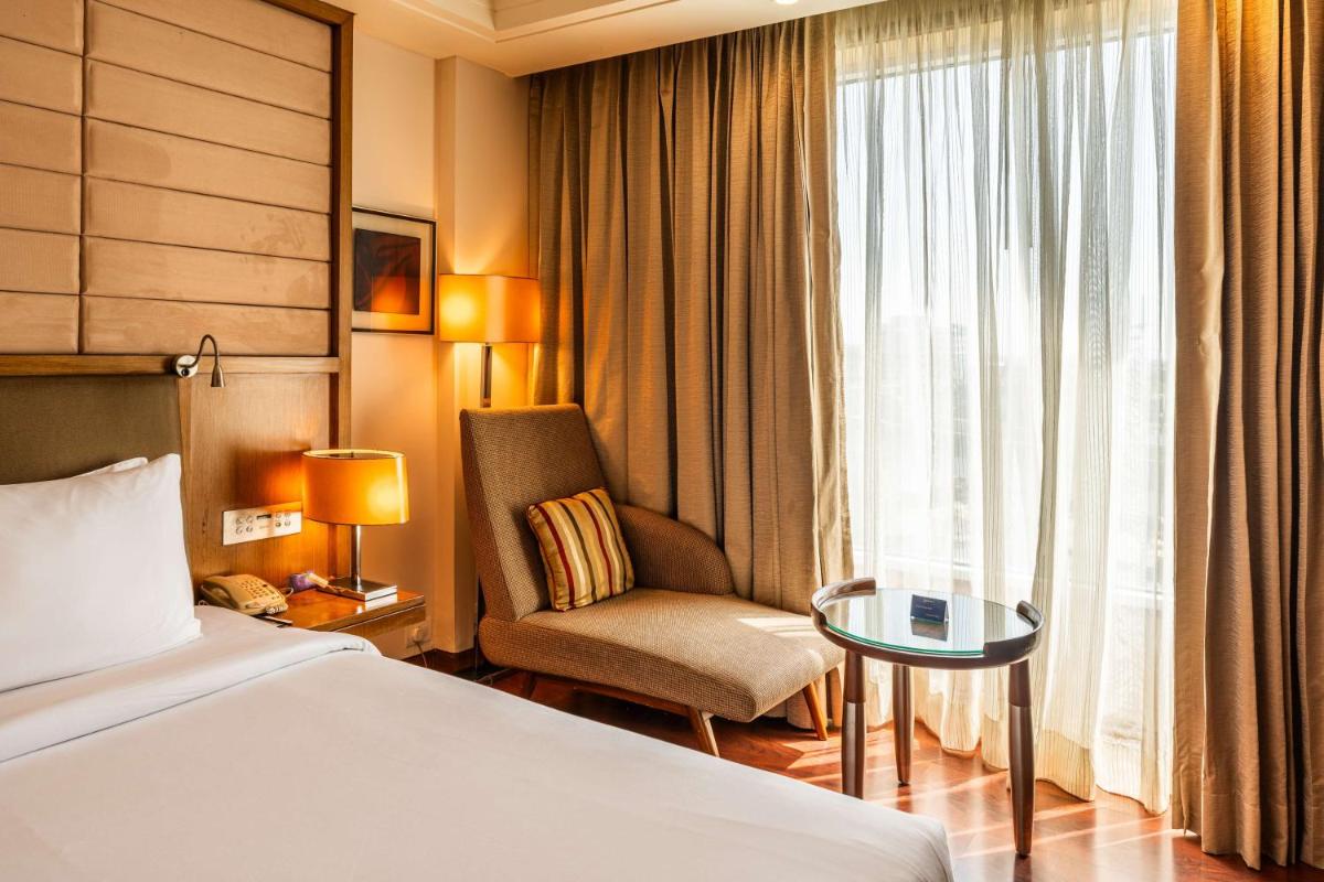 a hotel room with a bed and a chair and a window at Radisson Blu Hotel, Indore in Indore