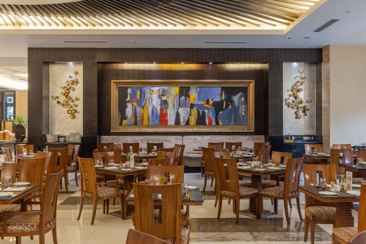 a dining room with tables and chairs and a painting at Radisson Blu Hotel, Indore in Indore