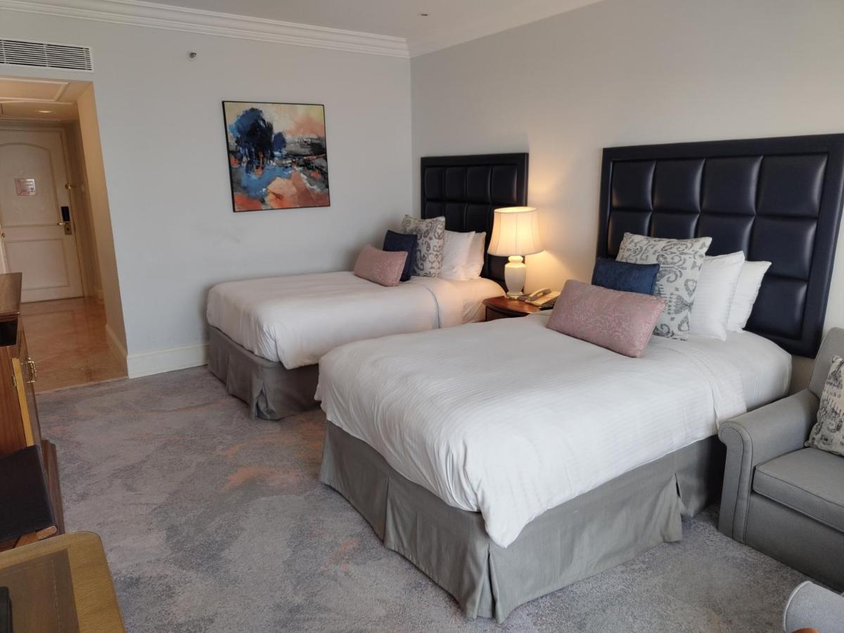 a hotel room with two beds and a chair at Taj Lands End in Mumbai a hotel room with two beds and a chair at Taj Lands End in Mumbai