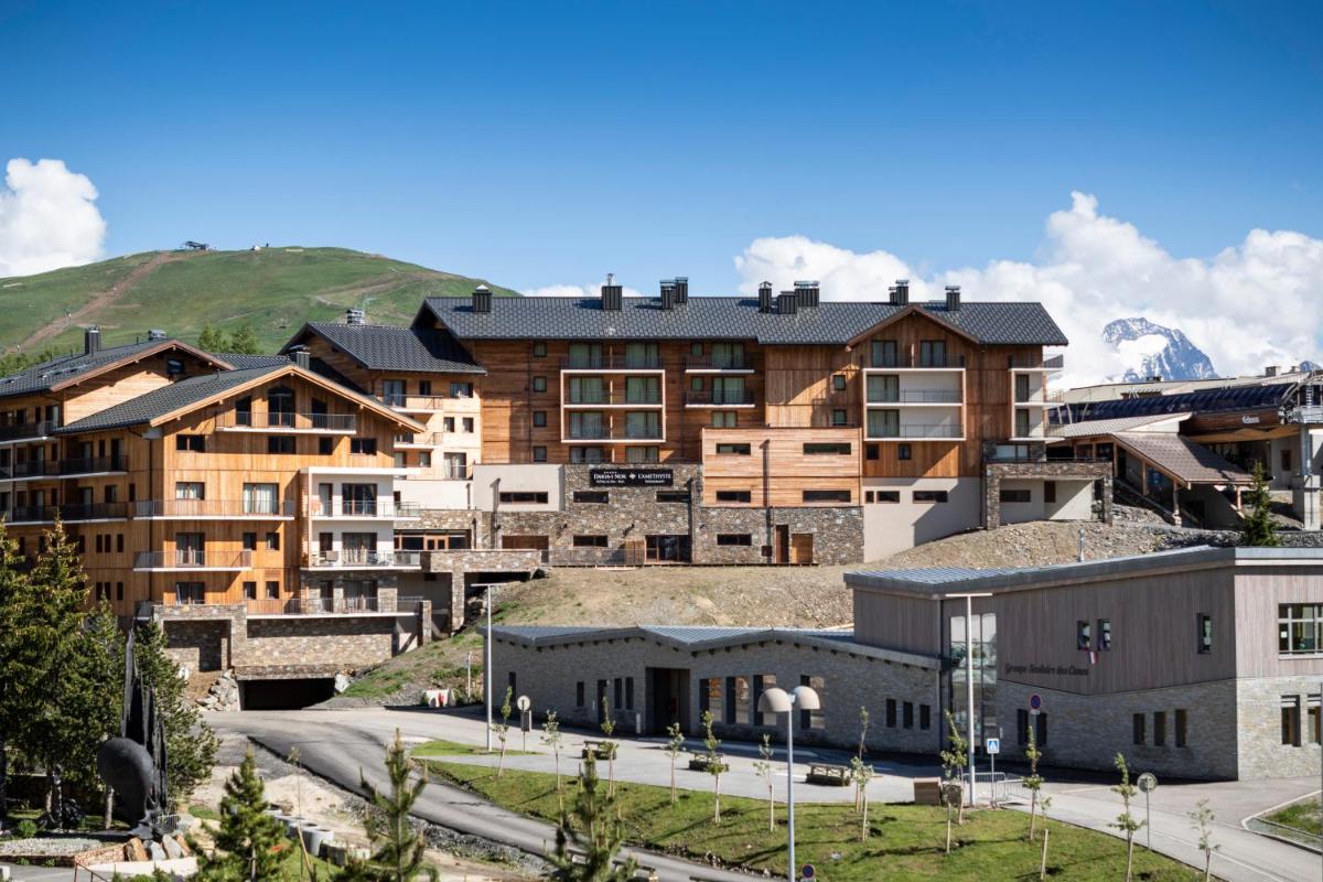 un groupe de bâtiments avec des montagnes en arrière-plan dans l'établissement Résidence Daria-I Nor by les Etincelles, à L'Alpe-d'Huez