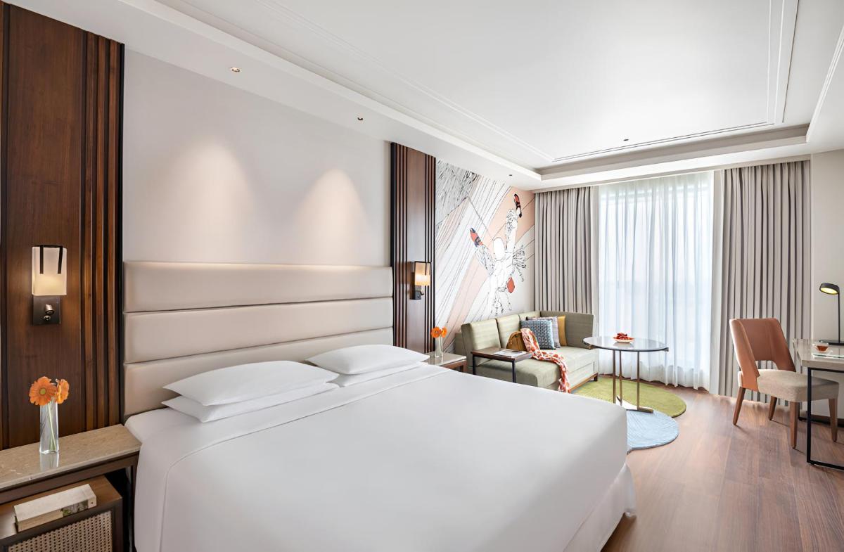 a bedroom with a white bed and a living room at Hyatt Centric Rajpur Road Dehradun in Dehradun