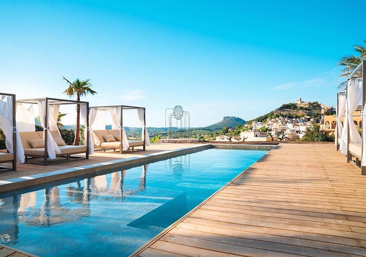 Una piscina en un resort con sillas y palmeras. en Hotel Creu de Tau Art&Spa-Adults only, en Capdepera