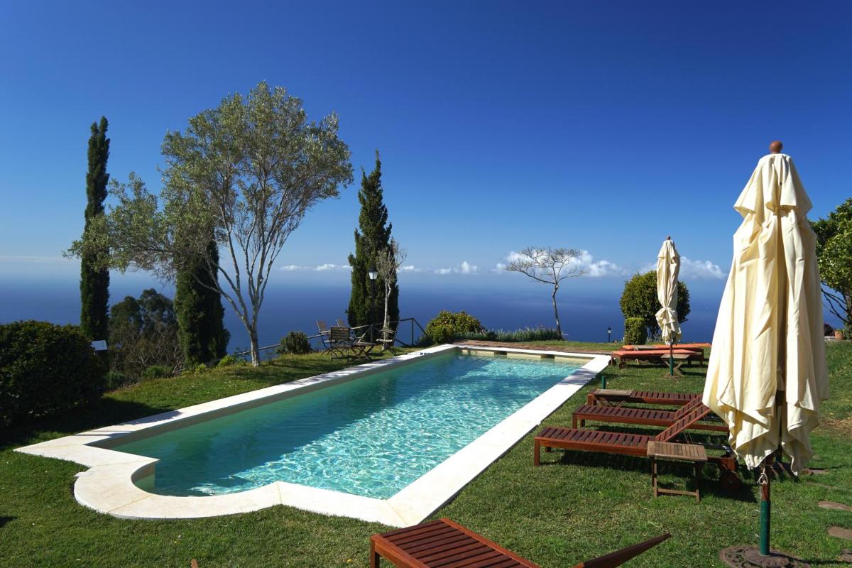uma piscina com cadeiras e um guarda-sol e o oceano em Atrio em Estreito da Calheta