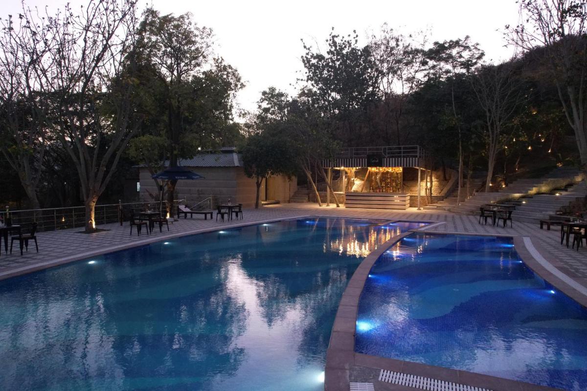 a large blue swimming pool with tables and chairs at Essentia Luxury Resort & Spa Udaipur in Udaipur