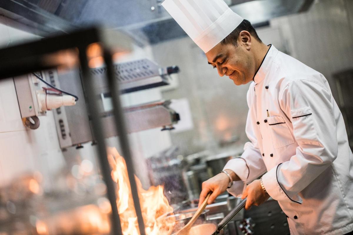a chef preparing food on a grill in a kitchen at Oakwood Residence Kapil Hyderabad in Hyderabad