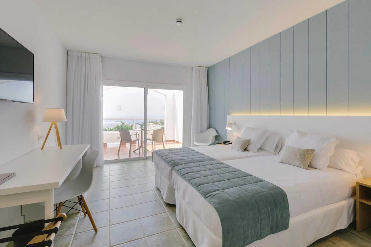 Un dormitorio con una cama y un escritorio y un balcón. en Alua Village Fuerteventura - All Inclusive, en Playa de Jandía