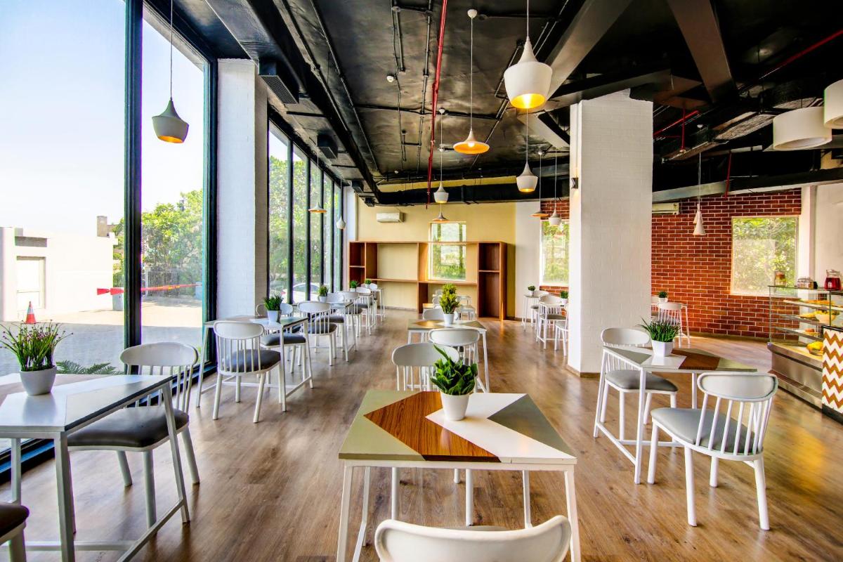 a restaurant with white tables and chairs and windows at Sunday Hotel Chandigarh Zirakpur in Zirakpur