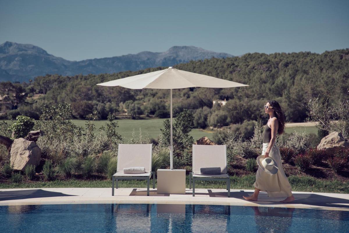 una mujer caminando por una piscina con sombrilla en Es Figueral Nou Hotel Rural & Spa - Adults Only - Over 12, en Montuiri