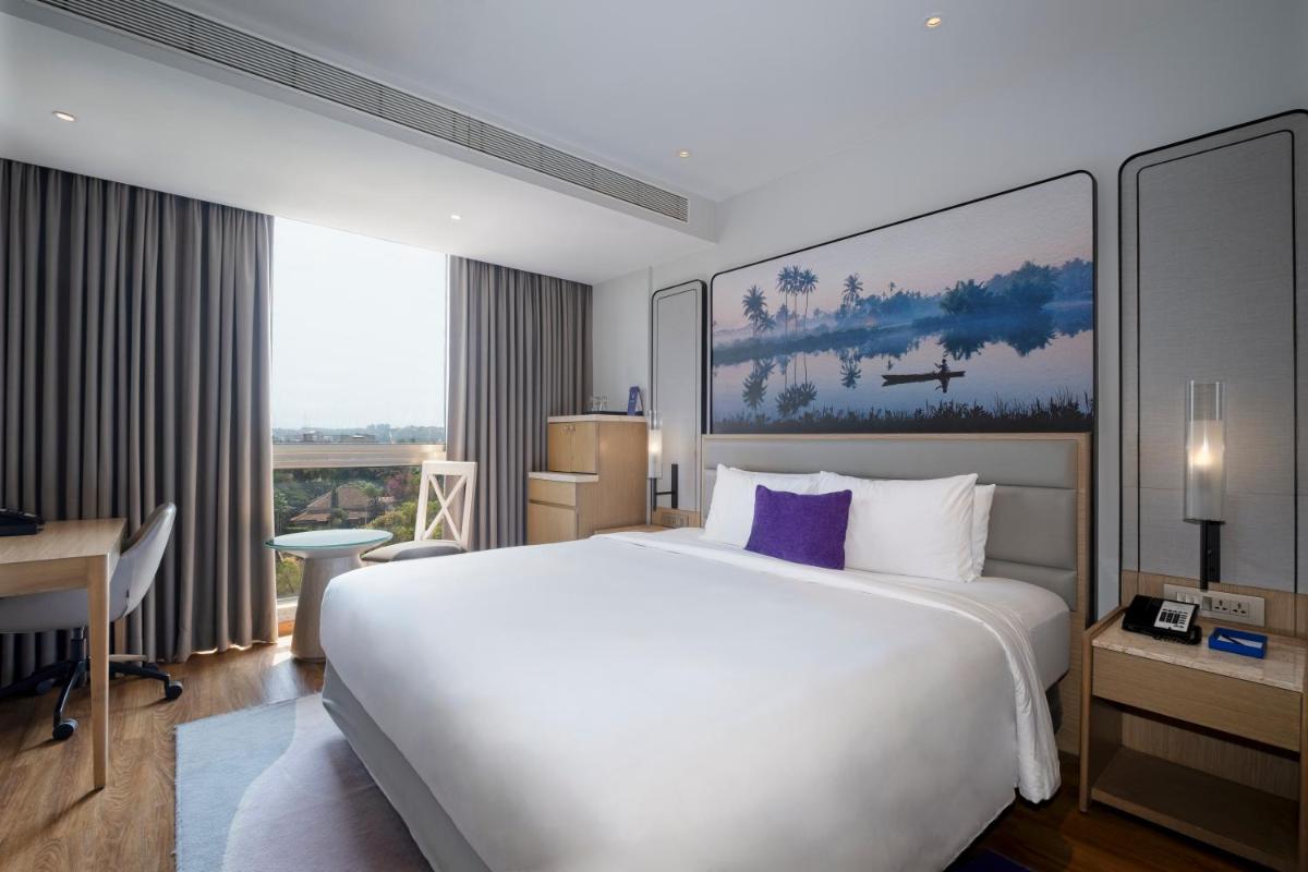 a hotel room with a large white bed and a desk at Vivanta Goa, Miramar in Panaji a hotel room with a large white bed and a desk at Vivanta Goa, Miramar in Panaji