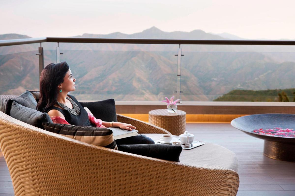 a woman sitting in a chair at a table with a view at JW Marriott Mussoorie Walnut Grove Resort & Spa in Mussoorie