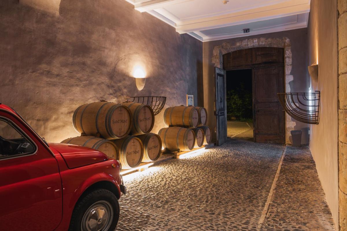 une rangée de tonneaux de vin dans un couloir avec une voiture rouge dans l'établissement Le Monastère de Saint Mont Hôtel & Spa, à Saint-Mont