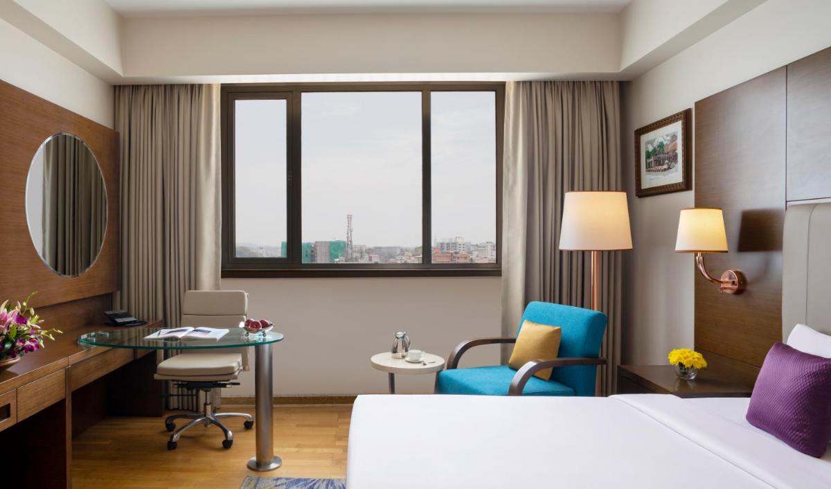 a hotel room with a bed and a desk and chair at Vivanta Thiruvananthapuram in Trivandrum