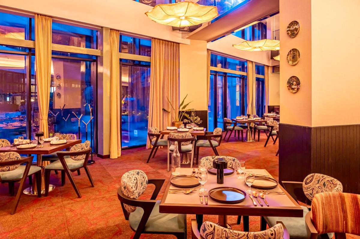 a restaurant with tables and chairs and windows at Novotel Kolkata Hotel and Residences in Kolkata a restaurant with tables and chairs and windows at Novotel Kolkata Hotel and Residences in Kolkata