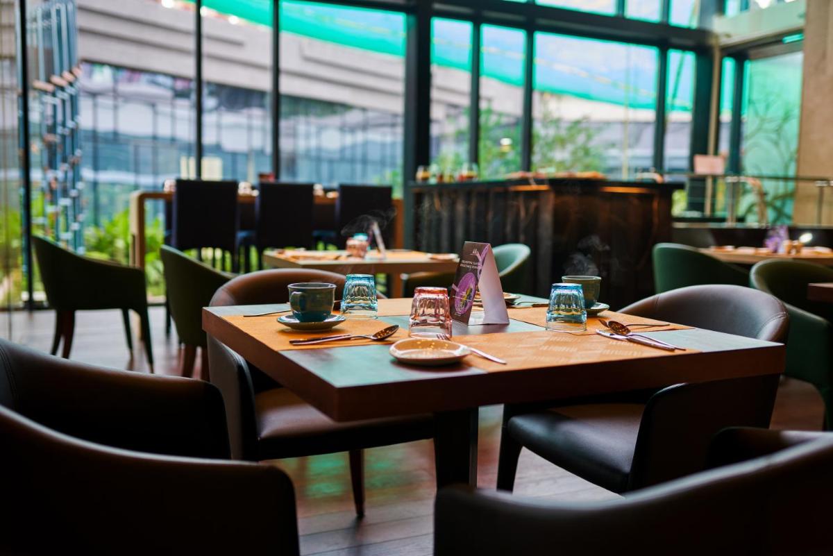 a restaurant with tables and chairs and windows at Novotel Kolkata Hotel and Residences in Kolkata a restaurant with tables and chairs and windows at Novotel Kolkata Hotel and Residences in Kolkata