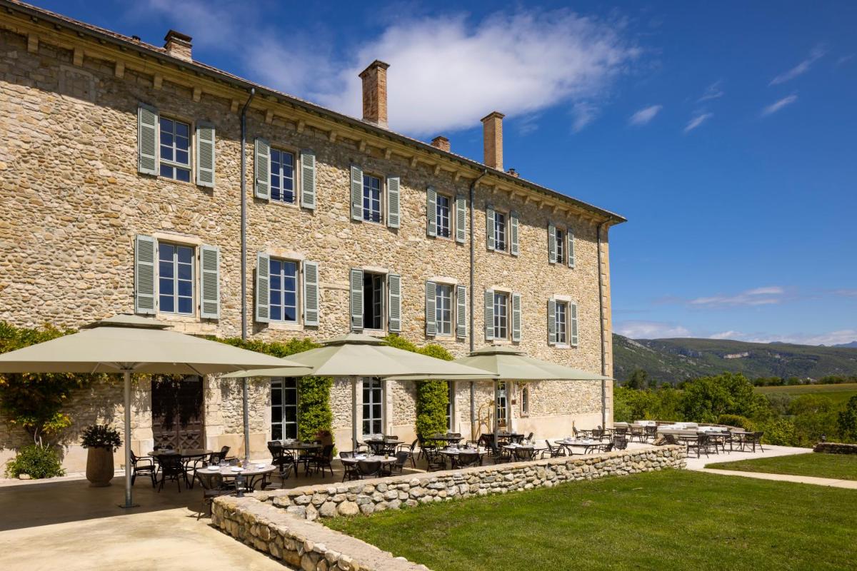 un grand bâtiment en briques avec des tables et des parasols dans l'établissement Château Les Oliviers de Salettes, à Charols