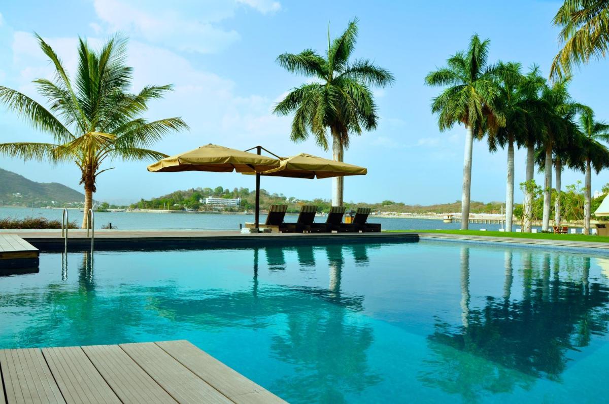 a swimming pool with palm trees and a view of the water at Hotel Lakend in Udaipur