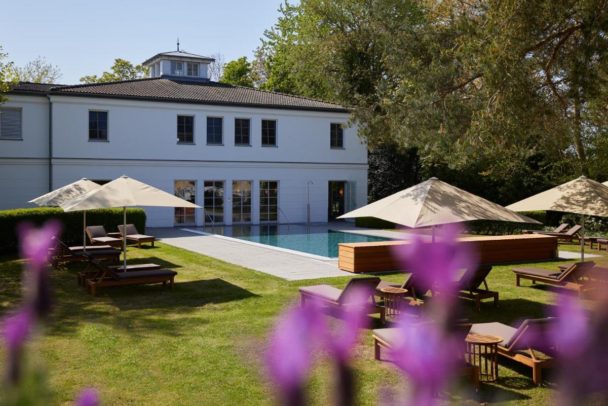 ein Gebäude mit einem Pool und Tischen und Stühlen und lila Blumen in der Unterkunft Strandhotel Zingst in Zingst