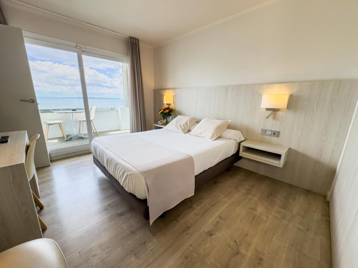 Un dormitorio con una gran cama blanca con una gran ventana. en Hotel Marina, en Roses