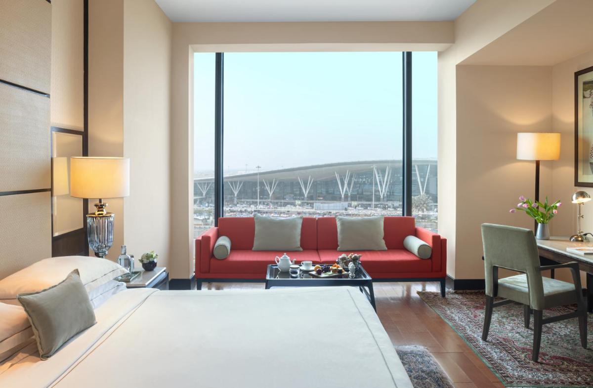 a living room with a red couch and a large window at Taj Bangalore in Devanahalli-Bangalore