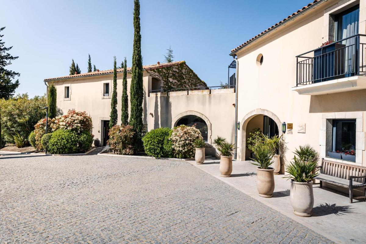 une allée devant un bâtiment avec des plantes en pot dans l'établissement Du Côté Des Olivades, à Paradou