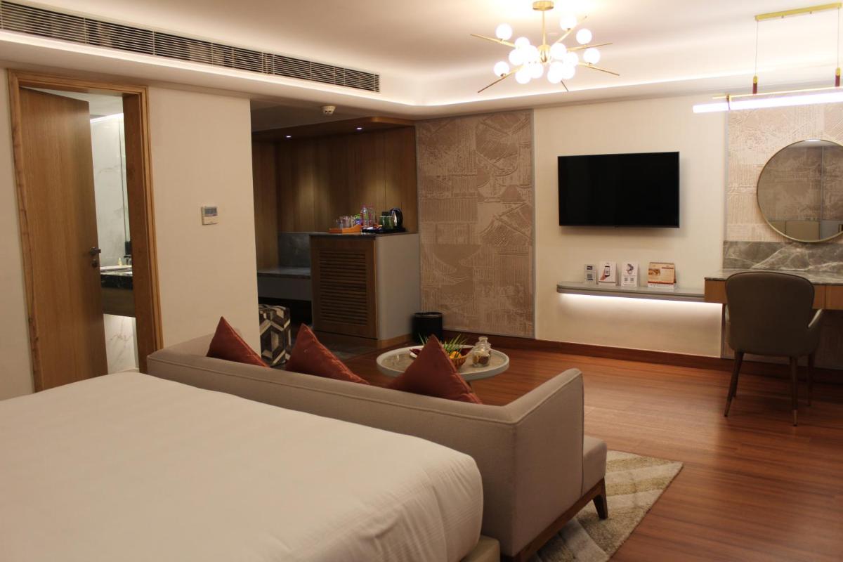 a bedroom with a bed and a living room with a tv at Pride Plaza Hotel, Ahmedabad in Ahmedabad