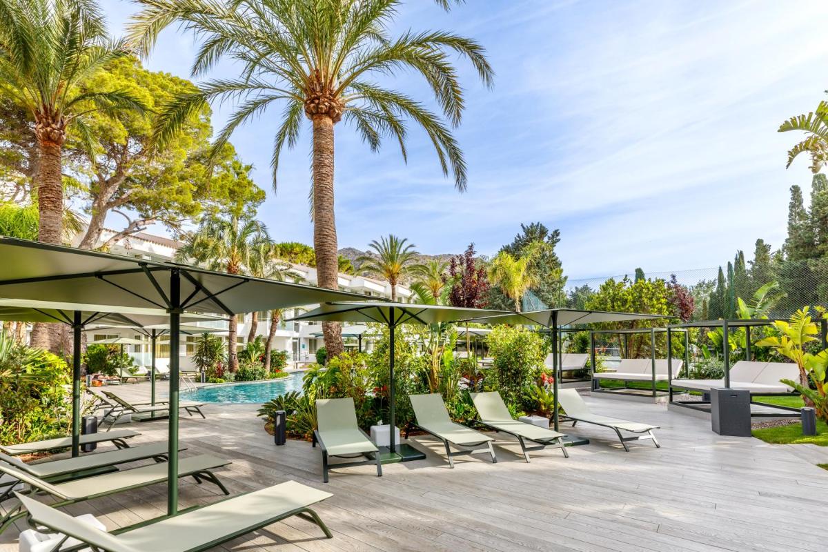 Un patio con tumbonas y palmeras. en Hotel Illa d'Or & Club Apts 4* Sup, en Puerto Pollensa