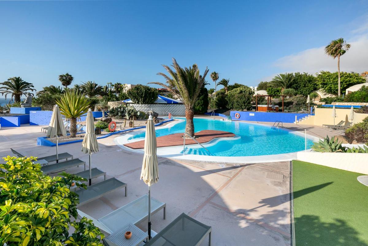 una piscina del complejo con sombrillas y palmeras en Hotel LIVVO Risco del Gato Suites, en Costa Calma