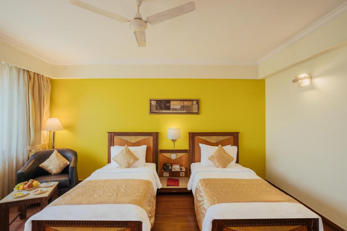 a hotel room with two beds and a chair at The Piccadily in Lucknow