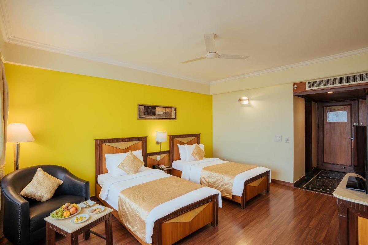 a hotel room with two beds and a chair at The Piccadily in Lucknow