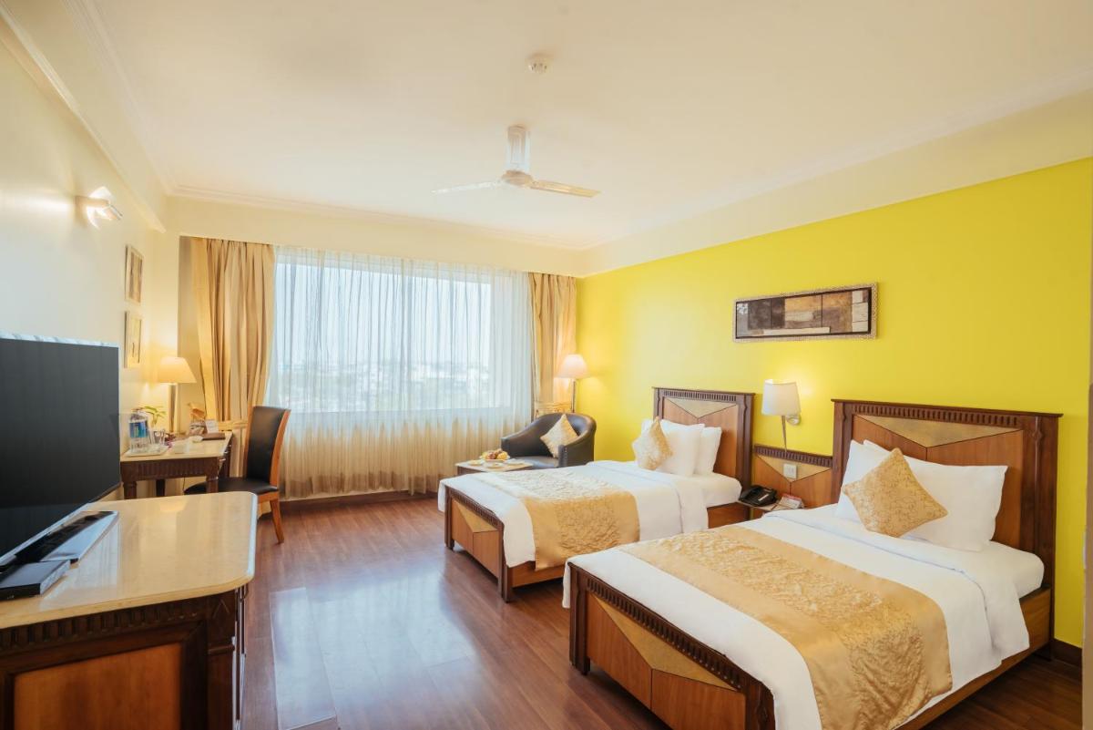 a hotel room with two beds and a desk at The Piccadily in Lucknow