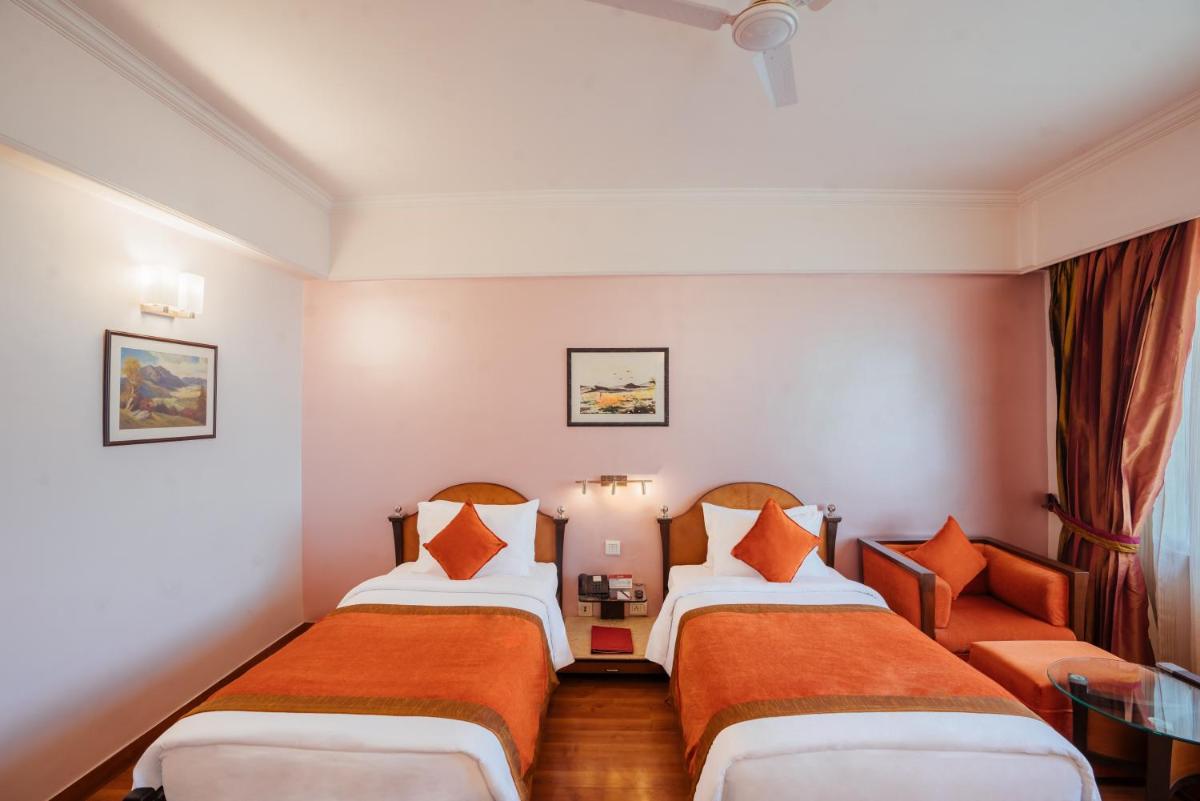 a hotel room with two beds with orange pillows at The Piccadily in Lucknow