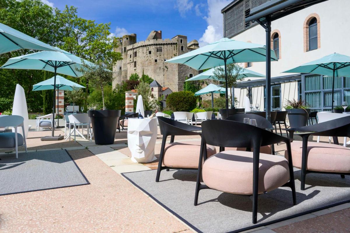 une terrasse avec des tables et des chaises, avec un château en arrière-plan dans l'établissement Best Western Plus Villa Saint Antoine Hotel & Spa, à Clisson