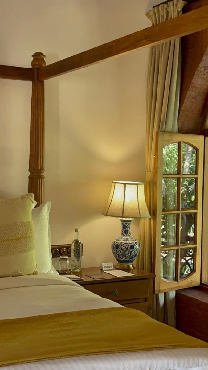 a bedroom with a bed with a lamp and a window at The Postcard Saligao in Calangute
