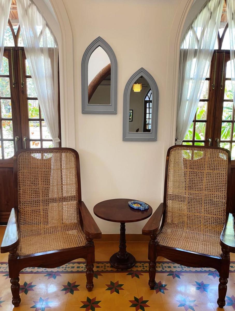 two chairs and a table in a room with windows at The Postcard Saligao in Calangute