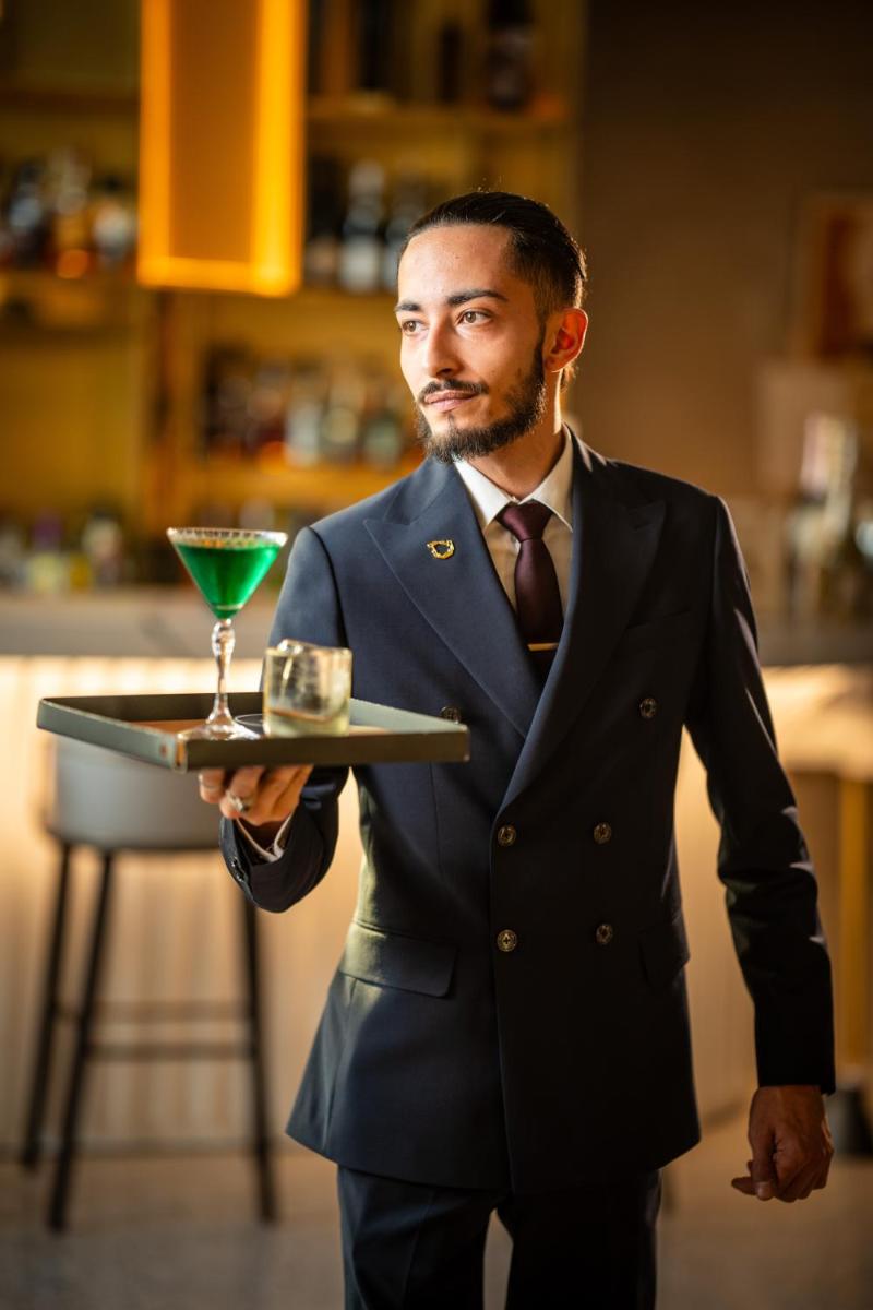 un homme en costume tenant un plateau avec une boisson dans l'établissement L'Esquisse Hotel & Spa Colmar - MGallery Collection, à Colmar 145 autres photos
