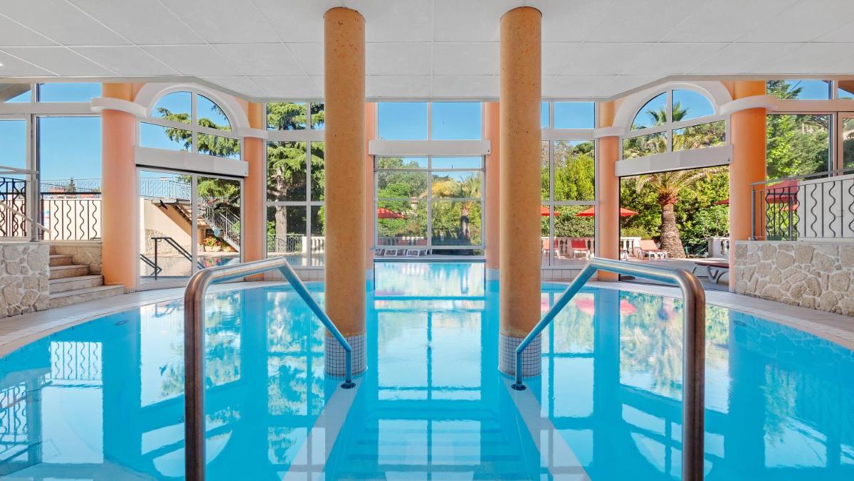 une piscine dans un hôtel avec de l'eau bleue et des fenêtres dans l'établissement Résidence les Tourelles, à Sainte-Maxime