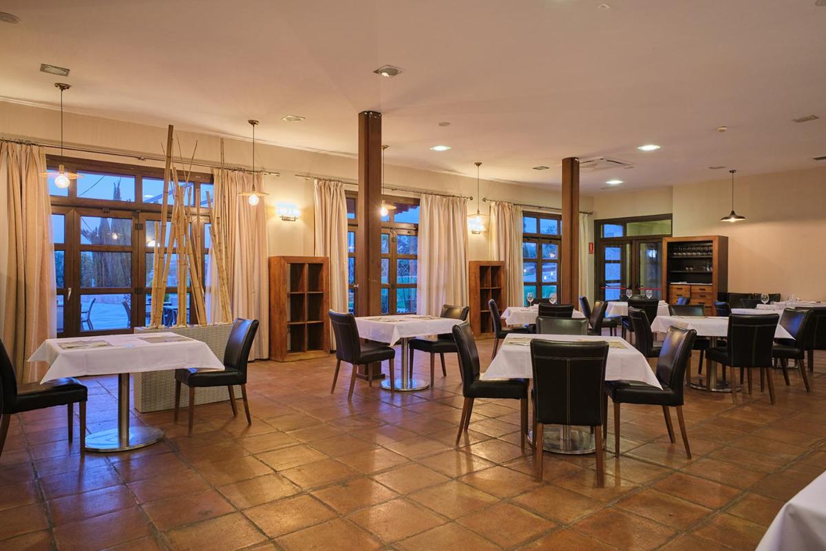Un restaurante con mesas y sillas blancas y ventanas. en Hotel Spa Villa Nazules, en Chueca