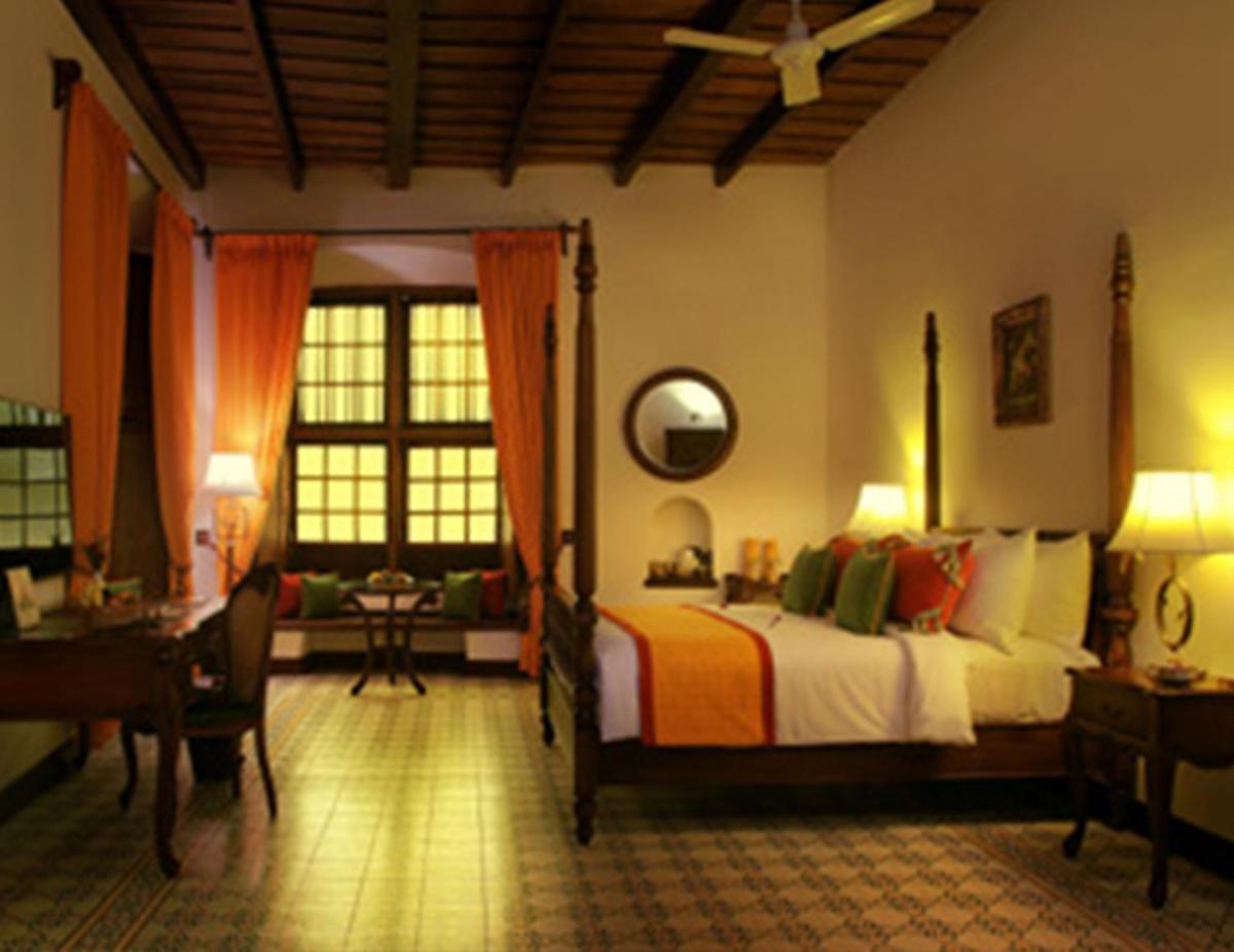 a bedroom with a bed and a desk and a room with a bed sidx sidx at Forte Kochi in Cochin
