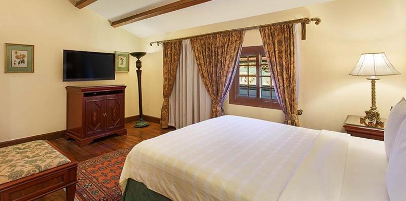 a bedroom with a large white bed and a television at The Oberoi Cecil in Shimla