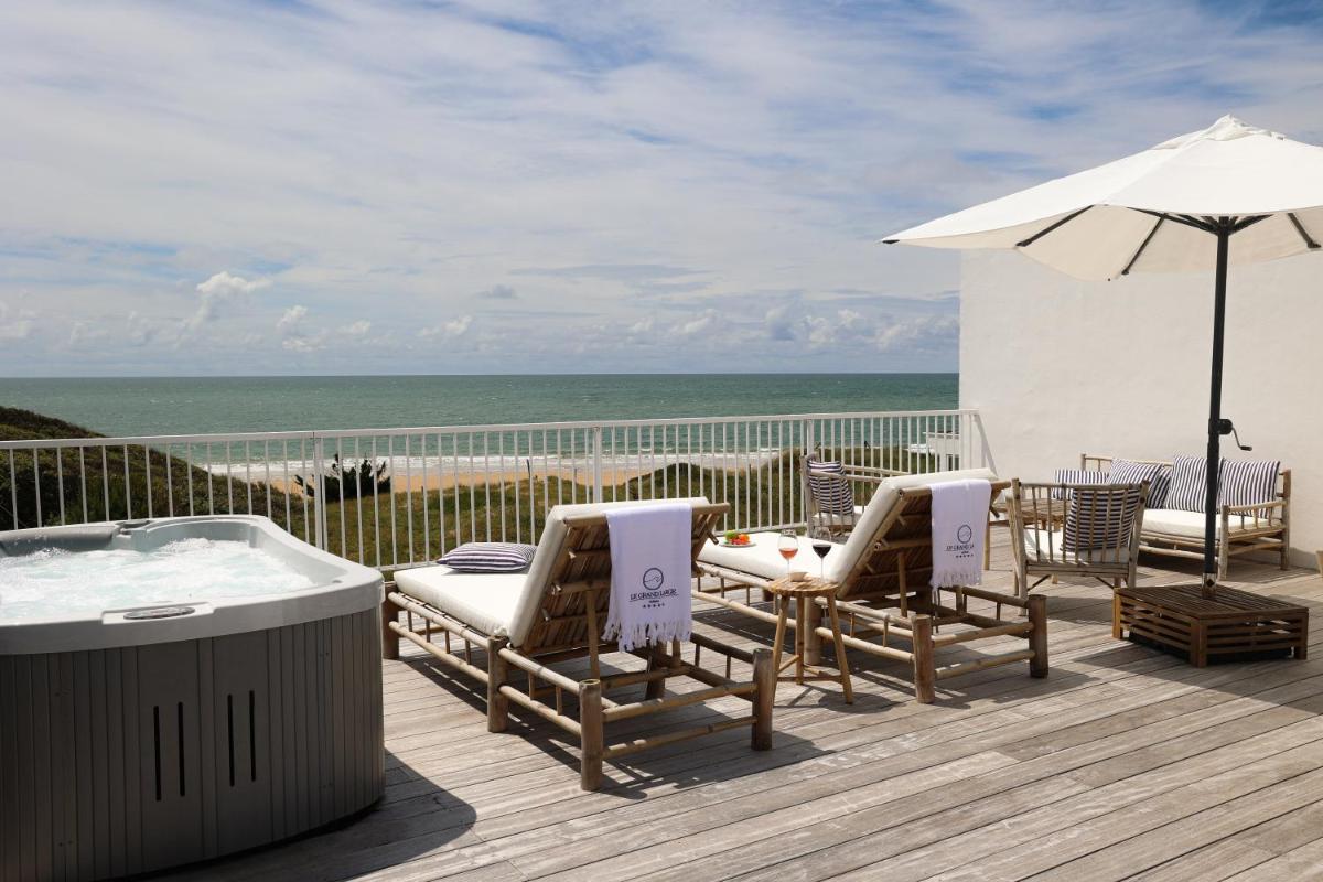 une terrasse avec un bain à remous, des chaises et un parasol dans l'établissement Hôtel & Spa Le Grand Large, à Dolus-d'Oléron