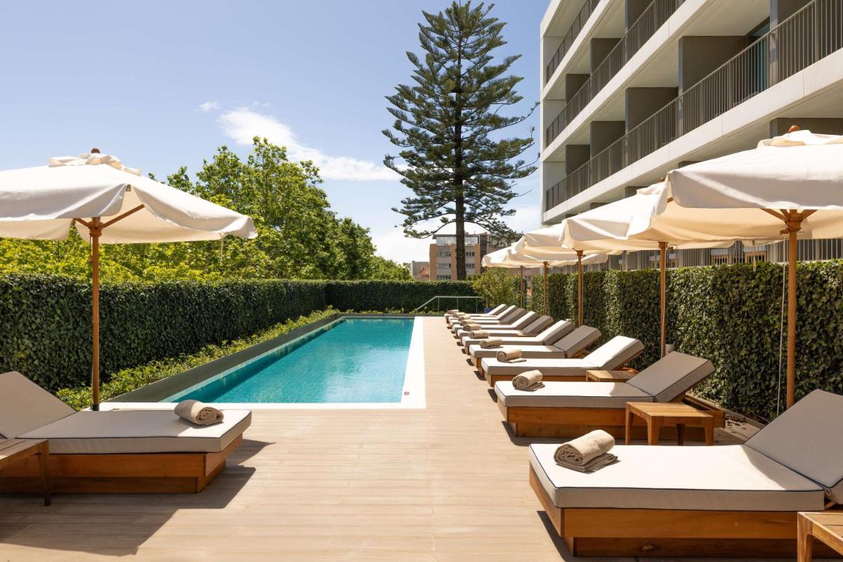 uma piscina com espreguiçadeiras e guarda-sóis ao lado de um edifício em Legacy Hotel Cascais, Curio Collection By Hilton em Cascais