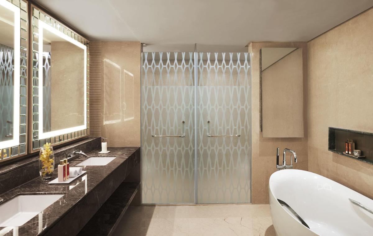 a bathroom with a shower and two sinks and a tub at Taj Santacruz in Mumbai