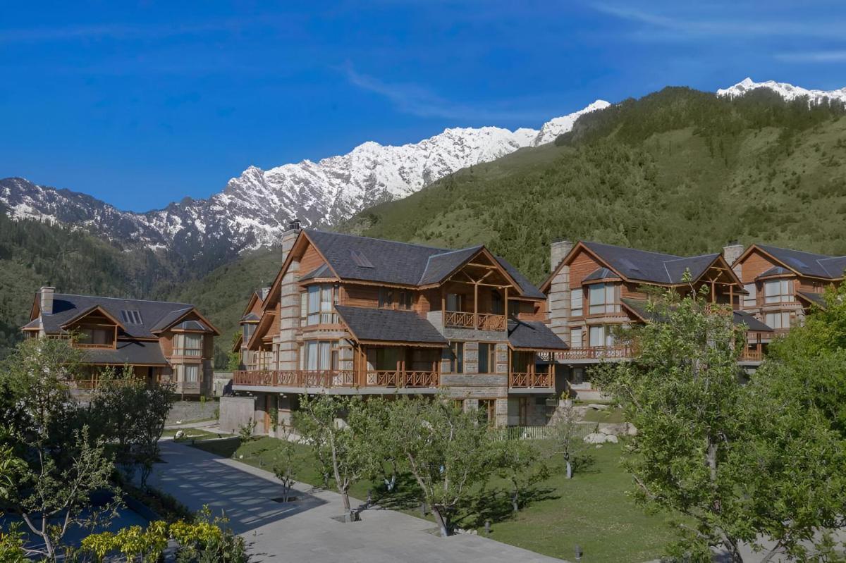 a large wooden house with mountains in the background at Welcomhotel By ITC Hotels, Hamsa Manali in Manāli a large wooden house with mountains in the background at Welcomhotel By ITC Hotels, Hamsa Manali in Manāli