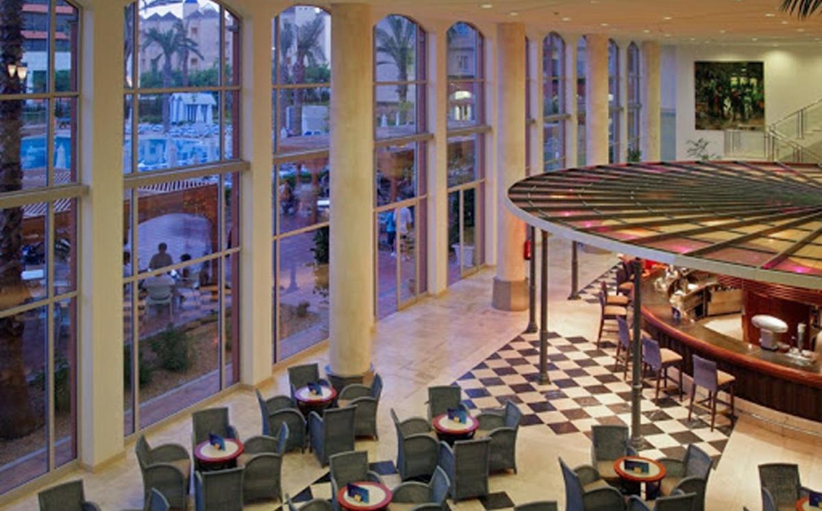 Un vestíbulo con sillas y mesas y grandes ventanales. en Ohtels Islantilla, en Islantilla