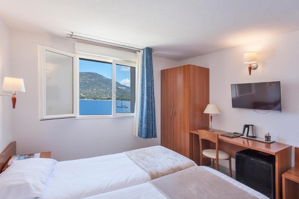 une chambre d'hôtel avec deux lits, un bureau et une fenêtre dans l'établissement Le Neptune & Spa, à Propriano