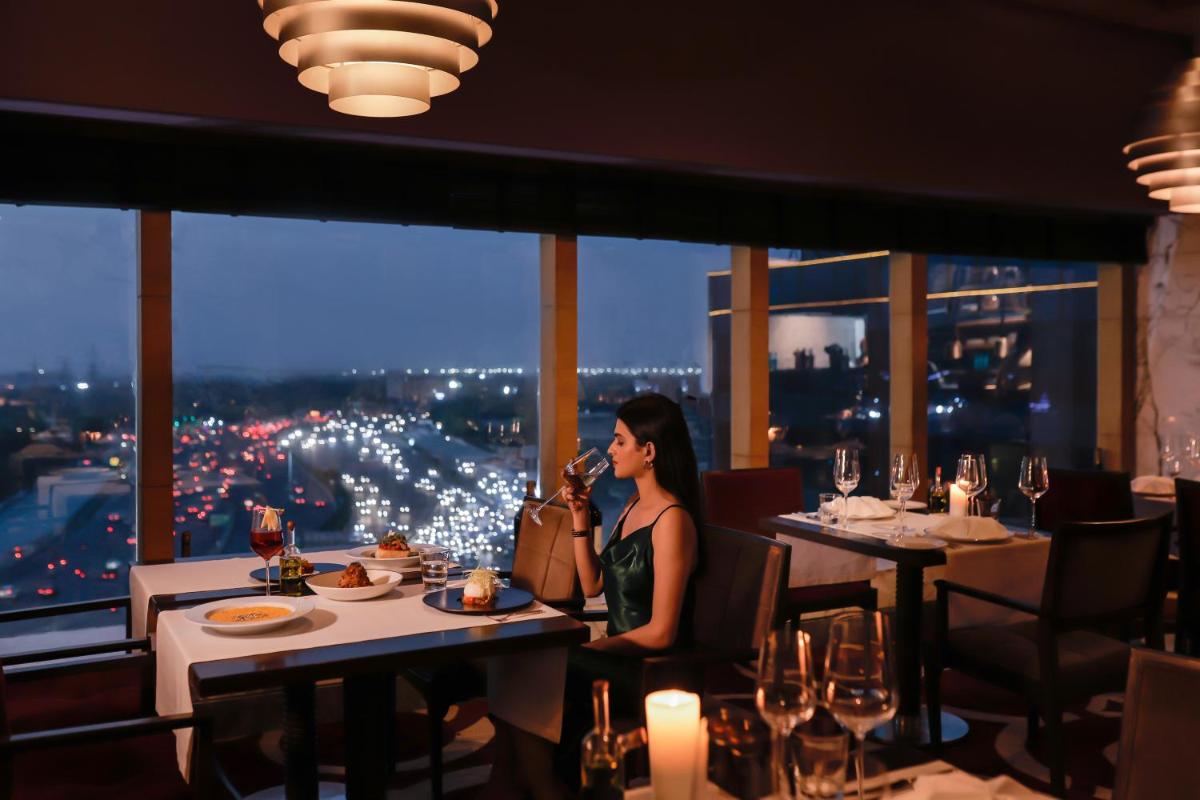 a woman sitting at a table in a restaurant at The Leela Ambience Gurugram Hotel & Residences - The Luxury Urban Sanctuary in Gurgaon