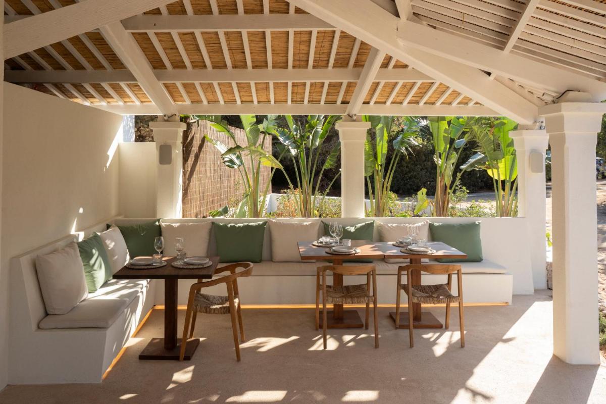 un patio con 2 mesas y sillas bajo una pérgola en Dunas de Formentera, a Small Luxury Hotel of the World, en Es Arenals